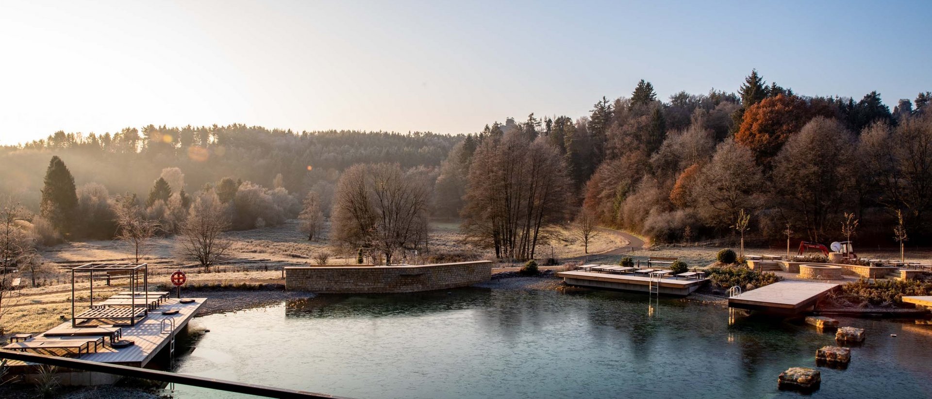Vereister Naturbadesee mit Liegeflächen und Bäumen im Herbst