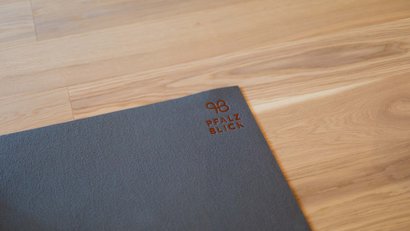 Ecke einer grauen Matte mit Pfalz Blick Logo auf einem Holzfußboden