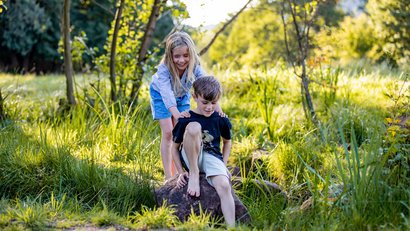 Mädchen hilft Jungen beim Klettern auf einen Felsen im Grünen