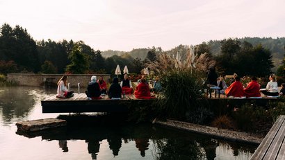 Groupe méditant dehors sur un ponton au bord du lac au lever du soleil