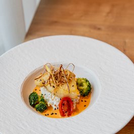 Kunstvoll angerichteter Fisch mit Brokkoli, Tomate und Sauce auf weißem Teller