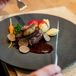 Gourmetgericht mit Steak, Trüffeln, Gemüsen und dunkler Sauce auf schwarzem Teller