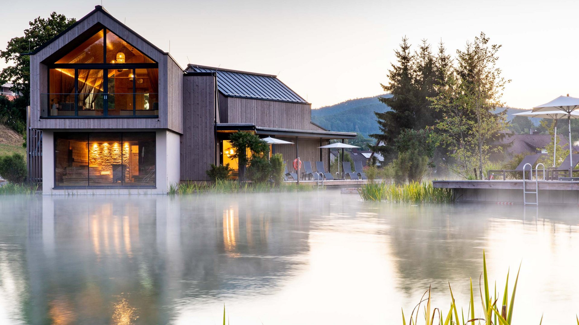 Modernes Haus am nebligen See mit Beleuchtung und Außenbereich