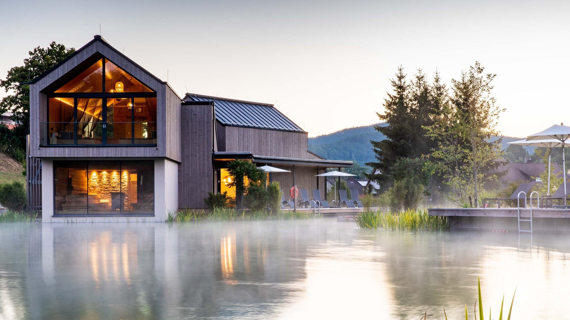 Maison moderne au bord d'un lac brumeux avec éclairage et terrasse