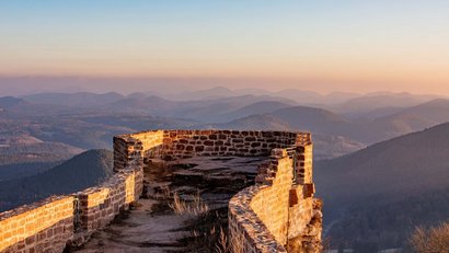 Ruine einer Burg mit Blick auf bewaldete Hügel im Sonnenuntergang