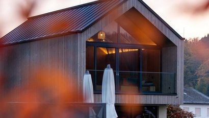 Modernes Holzhaus am Wasser mit herbstlichen Blättern im Vordergrund