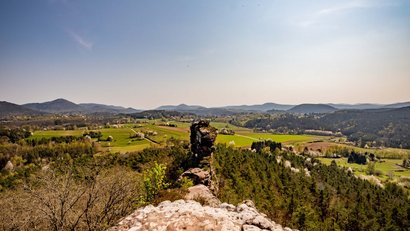 Blick über grüne Felder und Hügel bei klarem Himmel von einem felsigen Hügel aus
