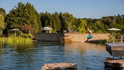 Junge springt in natürlichen Schwimmteich an sonnigem Tag