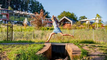 Kind springt über einen kleinen Graben im Freien bei Tageslicht