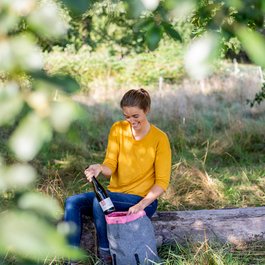 Femme en pull jaune sort une bouteille de vin d'un sac à dos en forêt