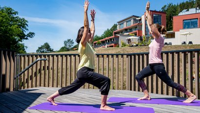Zwei Frauen machen Yoga auf einer Terrasse mit Aussicht auf moderne Gebäude
