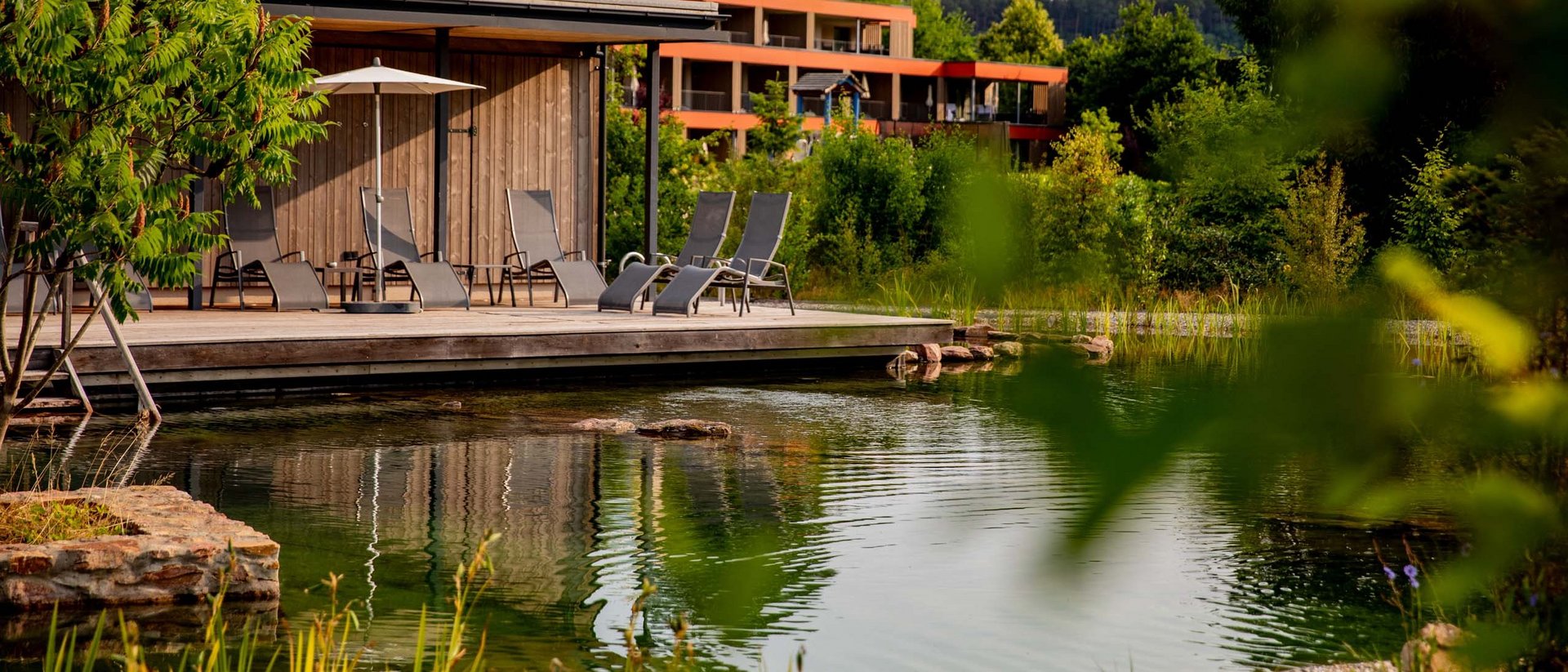 Holzterrasse mit Liegestühlen und Teich in einer grünen Wohnanlage