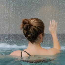 Frau von hinten im Pool, hebt eine Hand vor fallendem Wasser