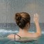 Frau von hinten im Pool, hebt eine Hand vor fallendem Wasser