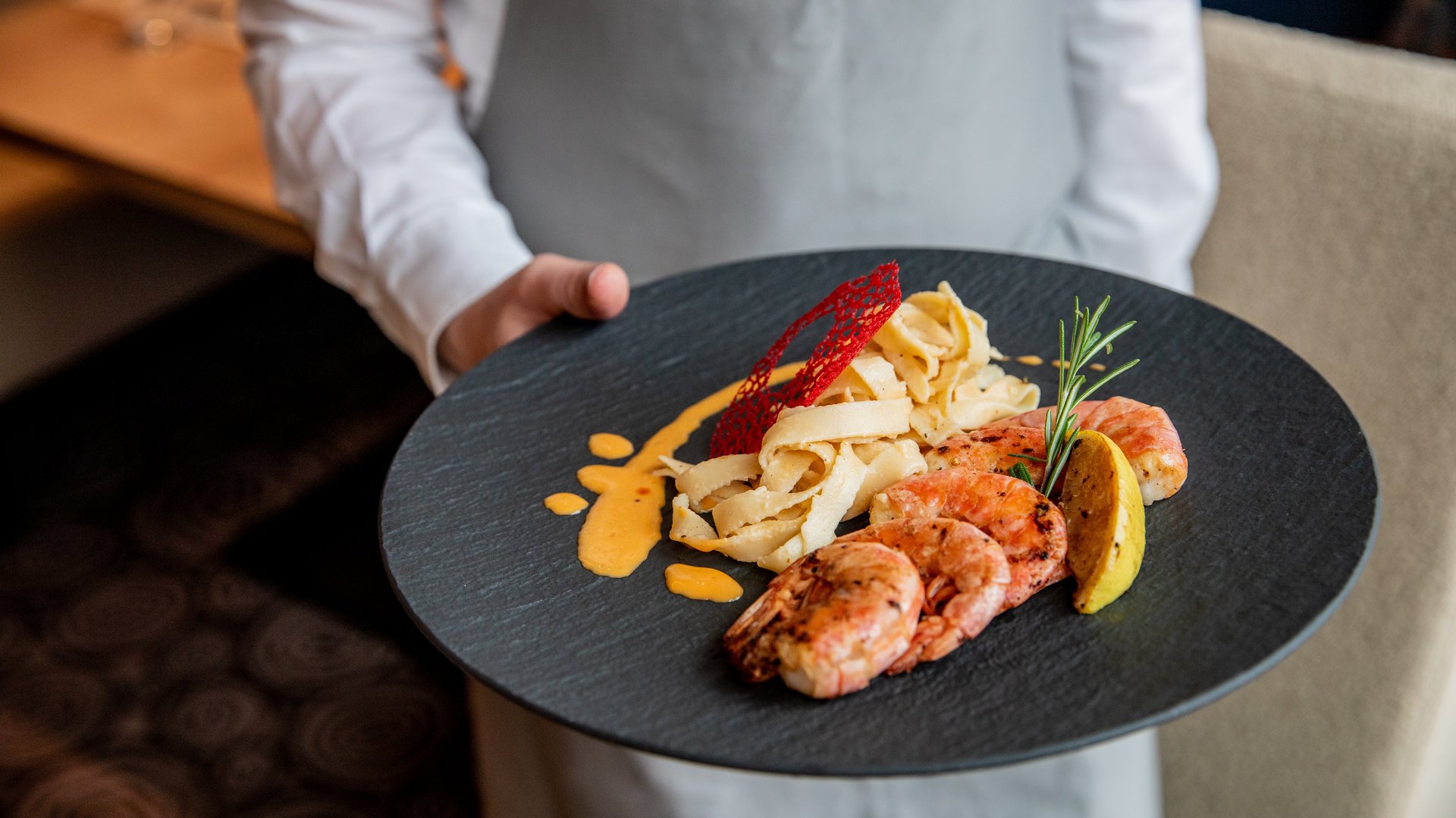 Koch hält Teller mit Pasta, Garnelen, Soße und Zitronenscheibe