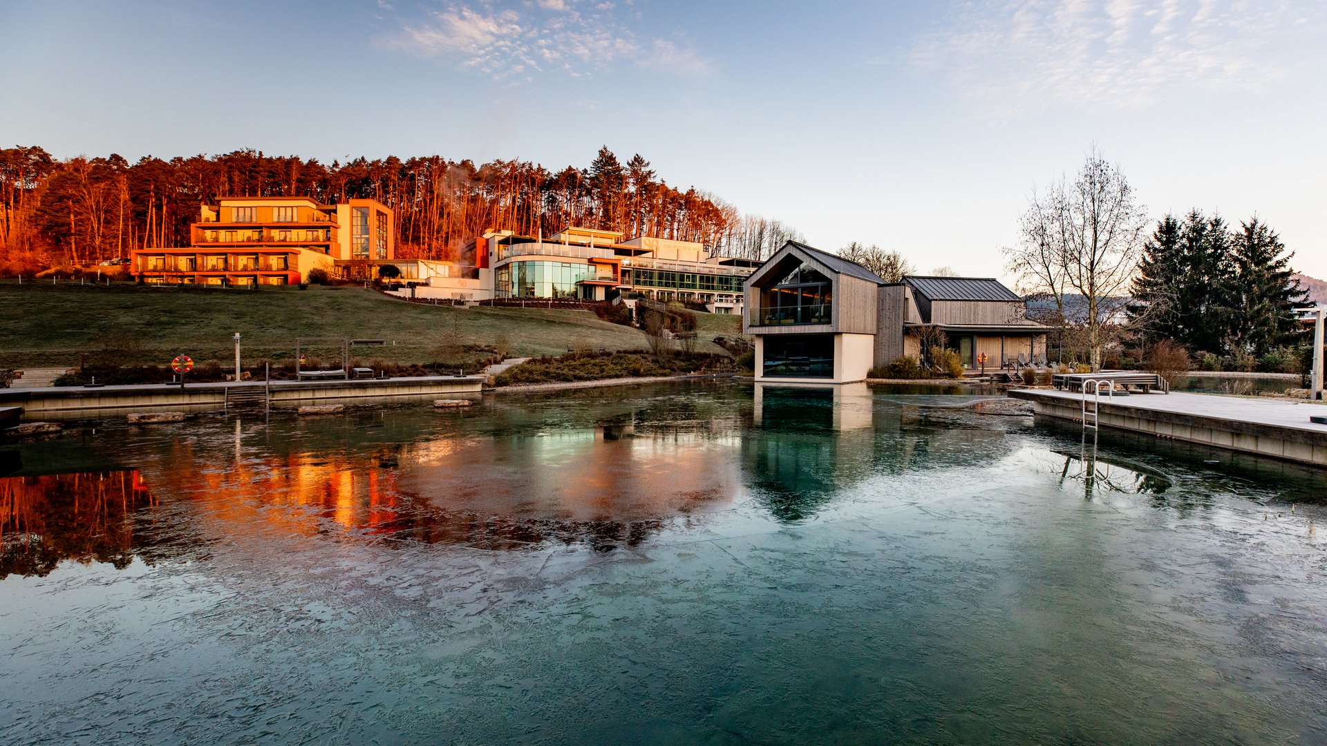 Moderne Gebäude am Ufer eines teils zugefrorenen Sees bei Sonnenuntergang