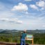 Kind zeigt auf Waldlandschaft mit Bergen unter blauem Himmel mit Wolken