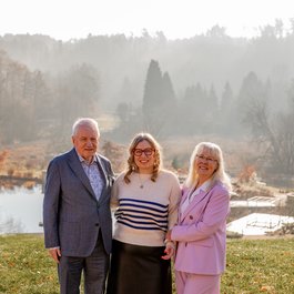 Drei Menschen lächeln zusammen im Park bei nebligem Wetter