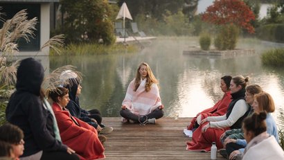 Gruppe meditiert auf Steg am See im Freien