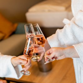Drei Hände stoßen mit Sektgläsern in Bademänteln an