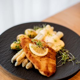 Schnitzel mit weißem Spargel, Kartoffeln und Sauce auf schwarzem Teller