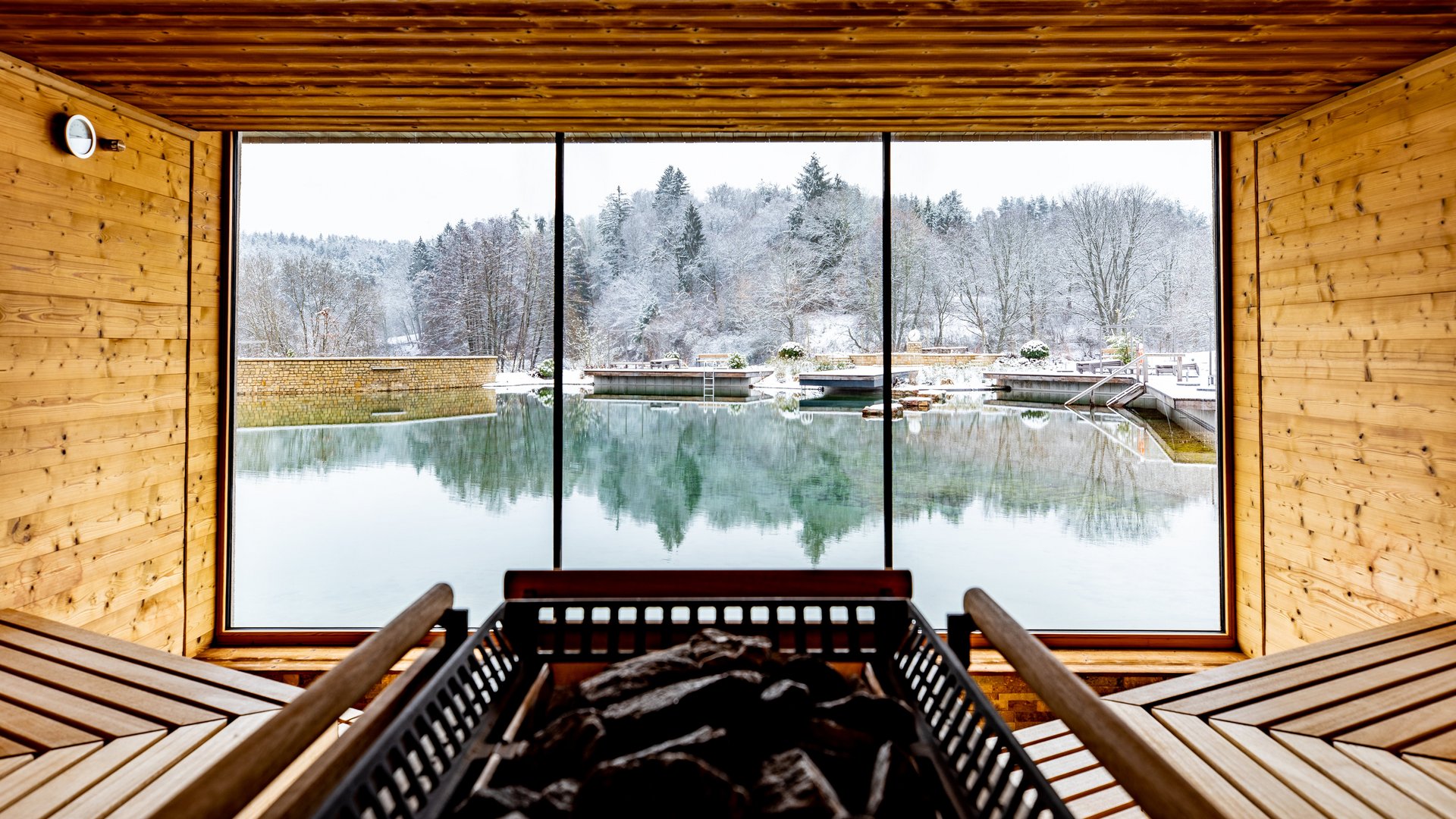 Intérieur d'un sauna avec vue sur des arbres enneigés et un plan d'eau