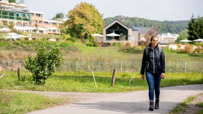 Frau wandert auf einem Weg in grüner Landschaft mit Haus und Hotel im Hintergrund