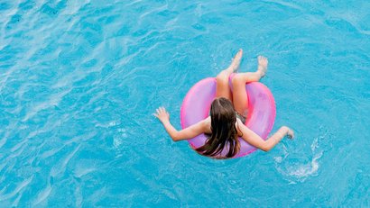 Child in a pink float ring relaxing in blue swimming pool water