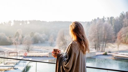 Femme avec tasse sur balcon regardant paysage hivernal avec lac